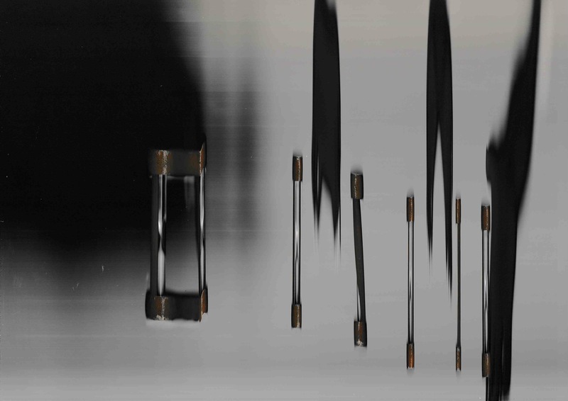 A small hourglass on a dark background represented seven times. It appears to roll across the image, surrounded by dark shadowy streaks. As it rolled across the platen, its form was compounded, elongated, and increasingly narrow.